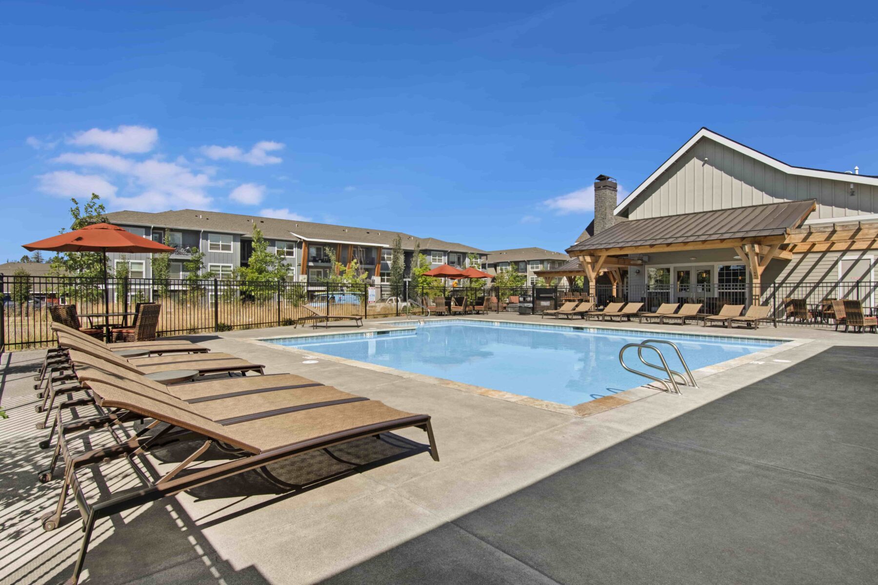 Swimming pool with lounge chairs, umbrellas, and clubhouse in background.