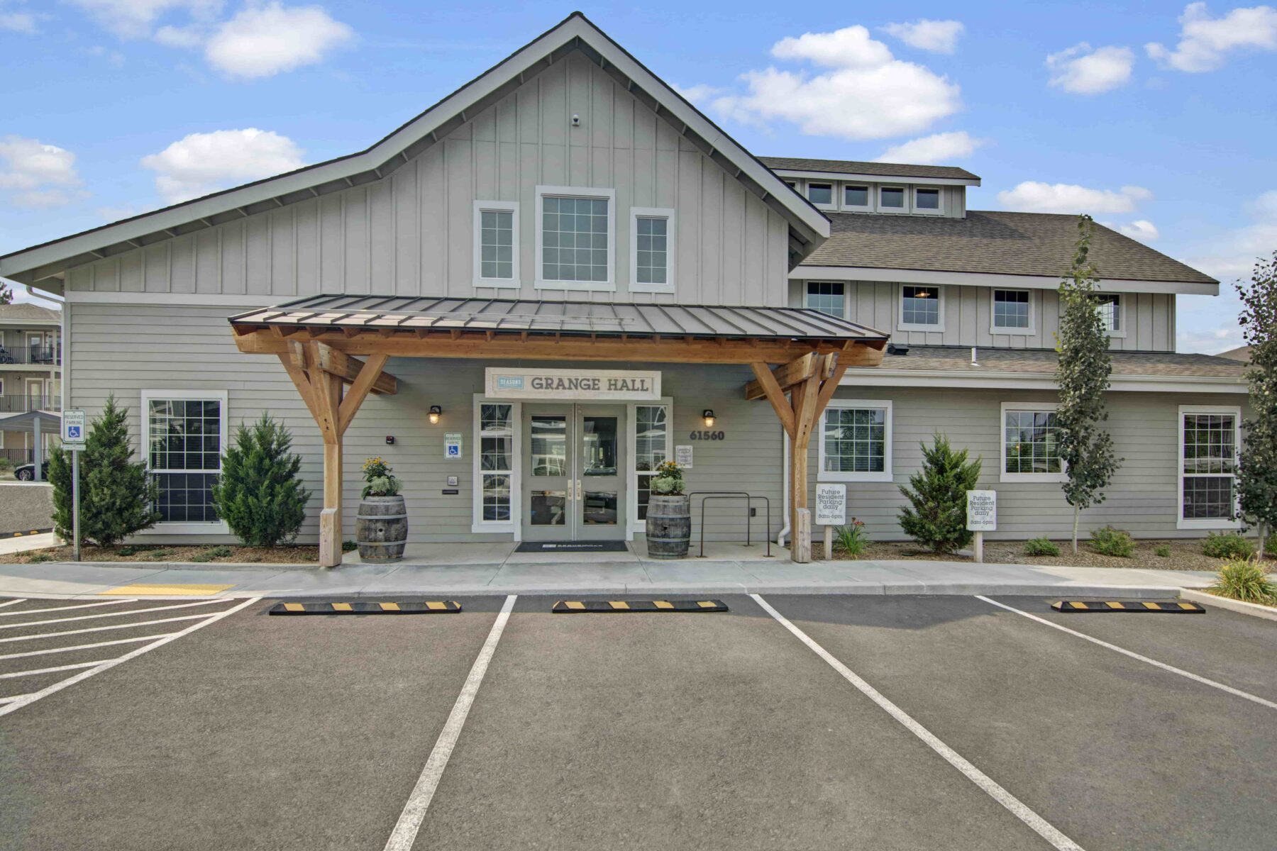 Large wooden building labeled ‘Grange Hall’ with peaked roof, covered porch, double door entrance, and large parking lot.