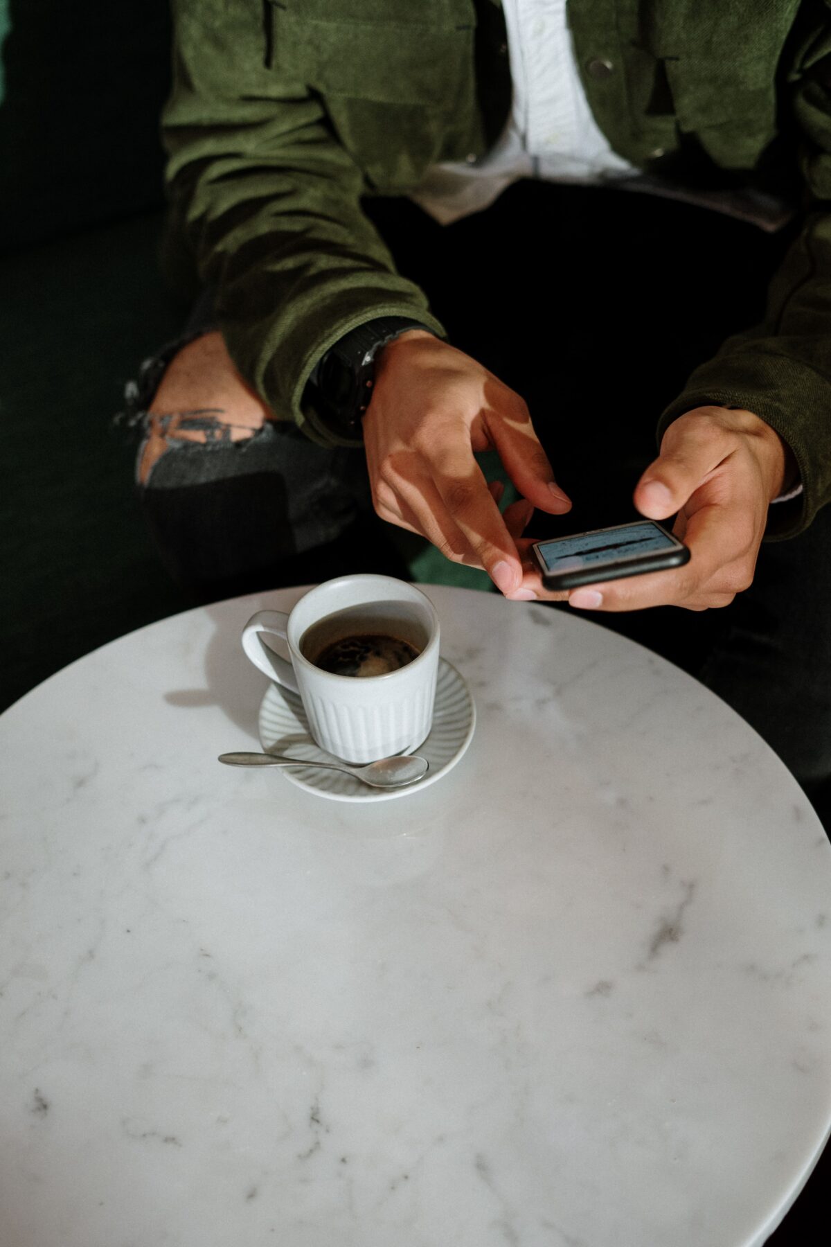 Man holding phone at table with cup of coffee and spoon